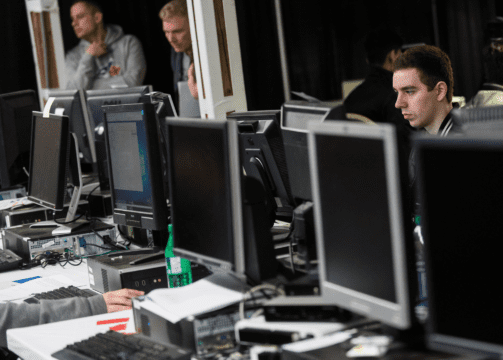 Computers lined up on a long office desk and some IT operators.