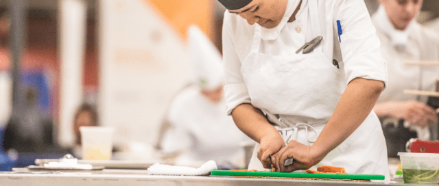 A chef using cooking tools on a vegetable cutting board